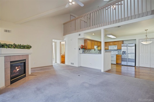 unfurnished living room featuring a tile fireplace, ceiling fan, light colored carpet, and a high ceiling