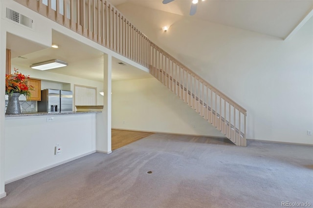 unfurnished living room featuring ceiling fan, a towering ceiling, and light colored carpet