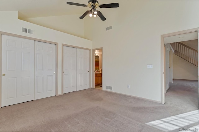 unfurnished bedroom featuring ceiling fan, light colored carpet, high vaulted ceiling, and ensuite bath