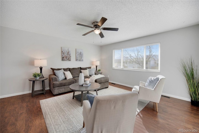 living room featuring dark wood-type flooring, ceiling fan, and a textured ceiling