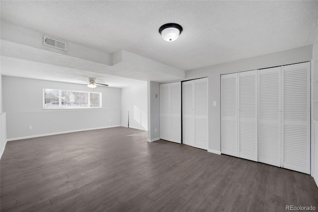 unfurnished bedroom featuring two closets, dark hardwood / wood-style floors, and a textured ceiling