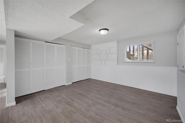 unfurnished bedroom featuring multiple closets, hardwood / wood-style floors, and a textured ceiling