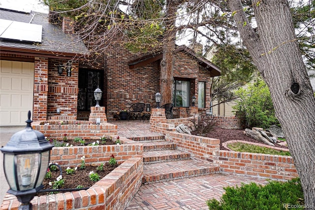 property entrance featuring brick siding, a chimney, and roof mounted solar panels