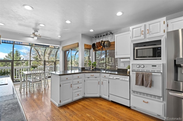 kitchen featuring a sink, light wood finished floors, a peninsula, stainless steel appliances, and white cabinetry