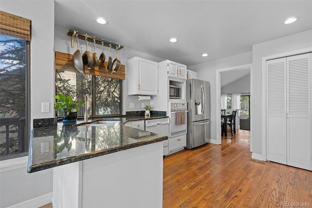 kitchen featuring appliances with stainless steel finishes, a sink, a peninsula, dark stone counters, and white cabinetry