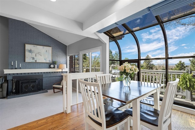 dining space featuring brick wall, wood finished floors, vaulted ceiling, and a fireplace