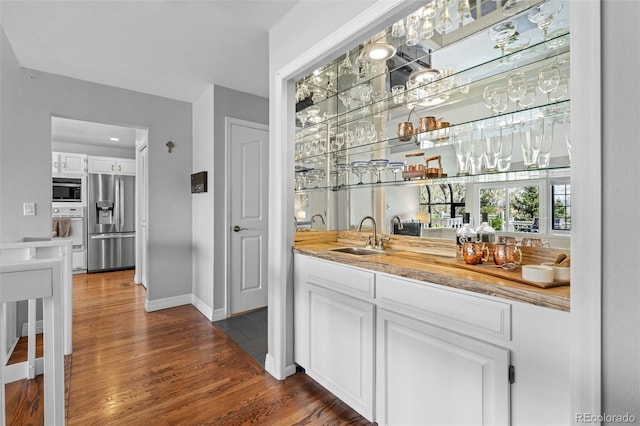 bar with a sink, indoor wet bar, stainless steel appliances, baseboards, and dark wood-type flooring