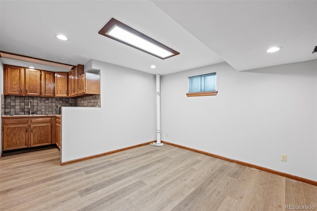 basement featuring recessed lighting, baseboards, a sink, and light wood-style floors