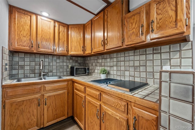 kitchen featuring black electric stovetop, tile counters, stainless steel microwave, tasteful backsplash, and a sink