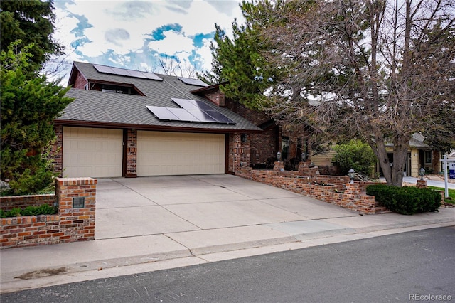 view of front of property with brick siding, driveway, roof mounted solar panels, and a garage