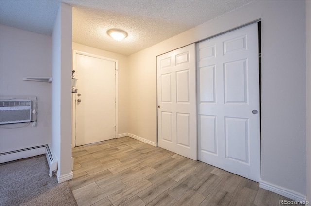 interior space with an AC wall unit, light hardwood / wood-style floors, a textured ceiling, and a baseboard heating unit