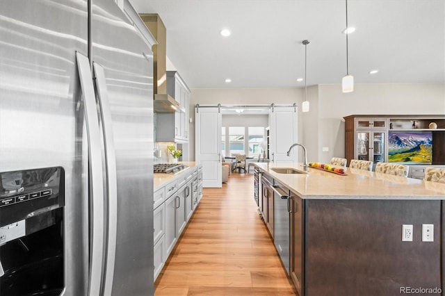kitchen with a large island with sink, light wood-type flooring, a barn door, appliances with stainless steel finishes, and a sink