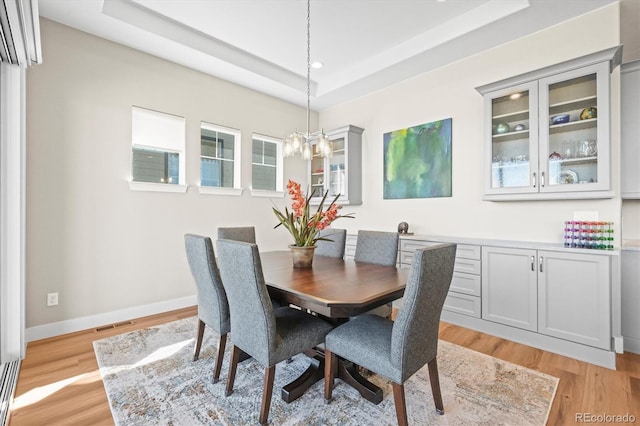 dining room with a raised ceiling, light wood finished floors, a notable chandelier, and visible vents