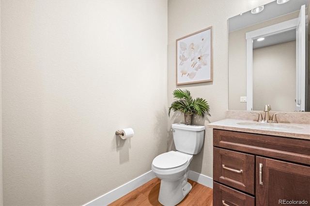 half bathroom featuring baseboards, wood finished floors, vanity, and toilet