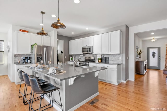 kitchen with pendant lighting, a kitchen island with sink, white cabinetry, appliances with stainless steel finishes, and a breakfast bar area