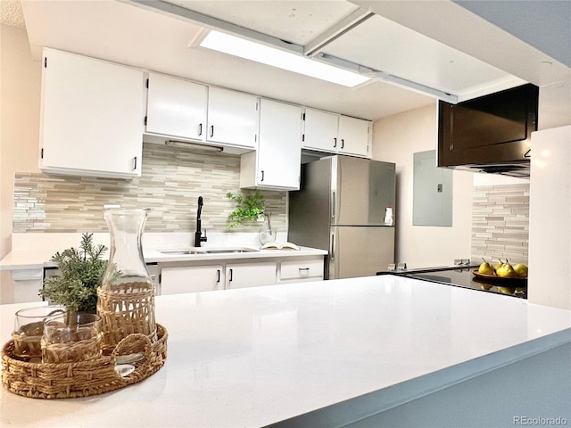 kitchen featuring freestanding refrigerator, electric panel, a sink, backsplash, and white cabinets