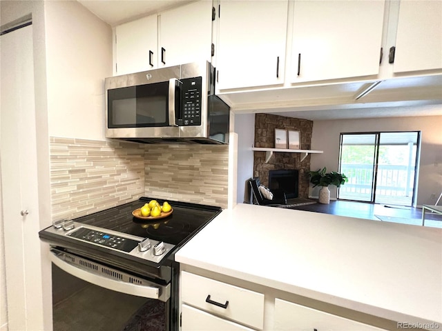 kitchen with stainless steel microwave, range with electric cooktop, backsplash, a stone fireplace, and white cabinetry