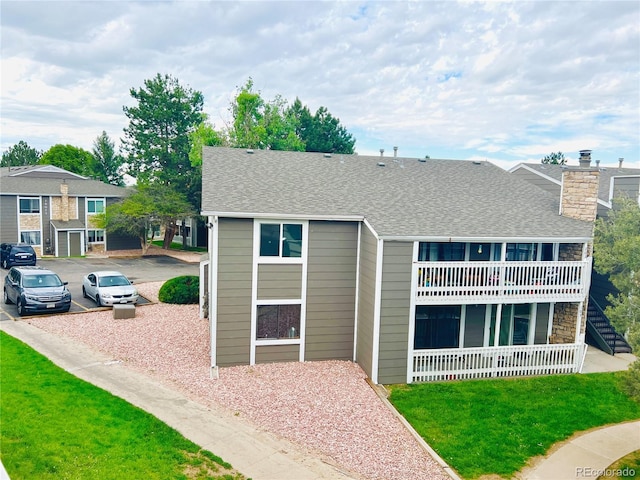rear view of house featuring roof with shingles, a yard, a balcony, and a chimney