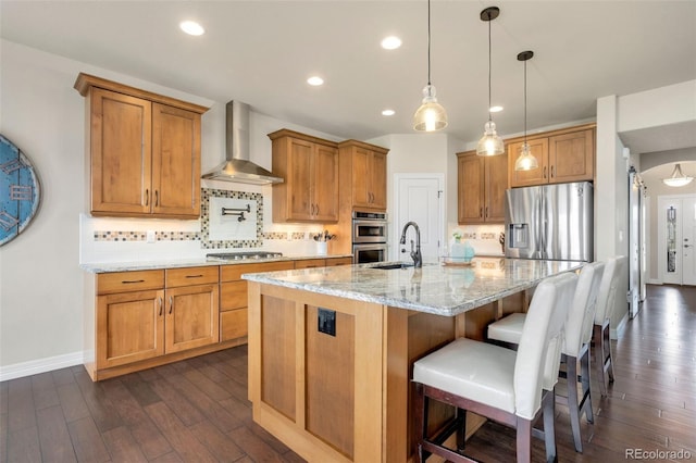 5954 Black Lion Ct, Windsor, CO 80550 - kitchen with wall chimney exhaust hood, appliances with stainless steel finishes, brown cabinetry, dark wood finished floors, and backsplash