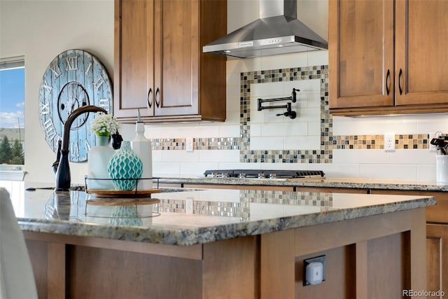 5954 Black Lion Ct, Windsor, CO 80550 - kitchen featuring wall chimney range hood, decorative backsplash, light stone countertops, and brown cabinets