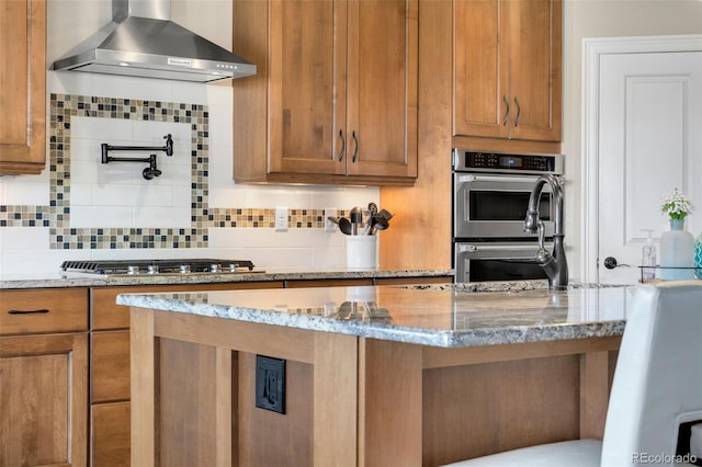 5954 Black Lion Ct, Windsor, CO 80550 - kitchen with wall chimney range hood, appliances with stainless steel finishes, light stone counters, and brown cabinetry