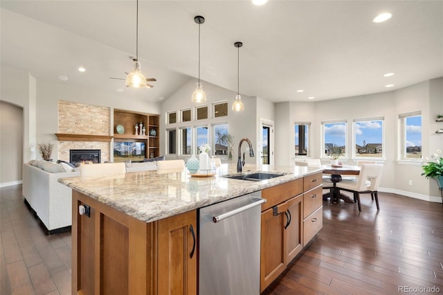 5954 Black Lion Ct, Windsor, CO 80550 - kitchen with dishwasher, a sink, brown cabinetry, an island with sink, and a fireplace