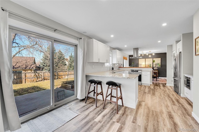 kitchen with a peninsula, a sink, appliances with stainless steel finishes, backsplash, and island range hood