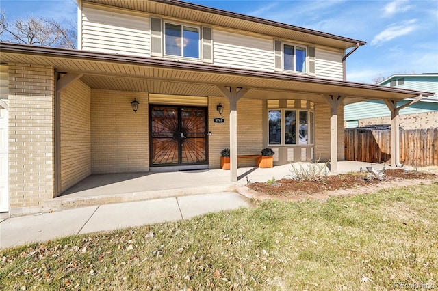 view of front facade featuring a porch, fence, and brick siding