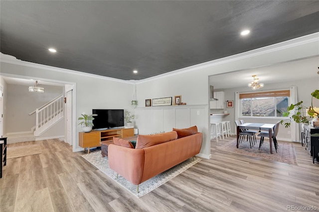 living room featuring stairway, an inviting chandelier, light wood-style flooring, and crown molding