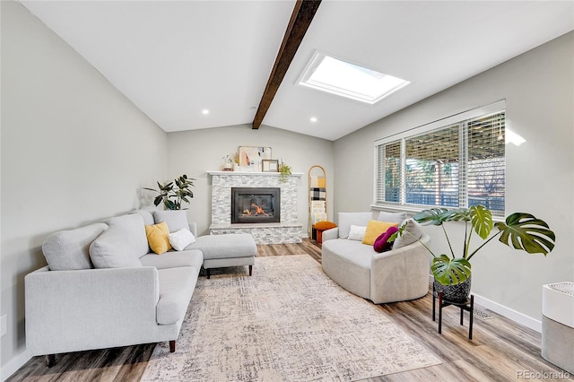 living area with a glass covered fireplace, vaulted ceiling with skylight, and wood finished floors