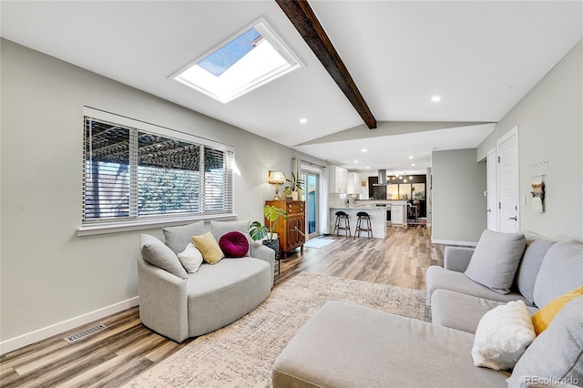 living room featuring vaulted ceiling with skylight, baseboards, visible vents, and light wood-type flooring