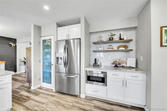 kitchen with light wood-type flooring, stainless steel refrigerator with ice dispenser, backsplash, white cabinetry, and light stone countertops