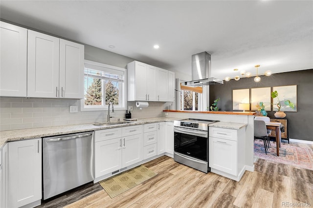 kitchen with a sink, island exhaust hood, light wood-style floors, appliances with stainless steel finishes, and a peninsula