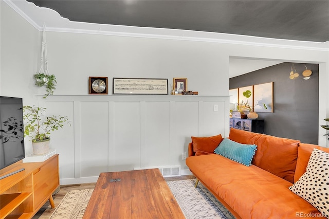 living room featuring a decorative wall, wood finished floors, visible vents, and ornamental molding