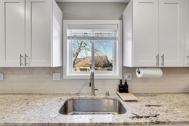 kitchen featuring white cabinetry, light stone counters, tasteful backsplash, and a sink