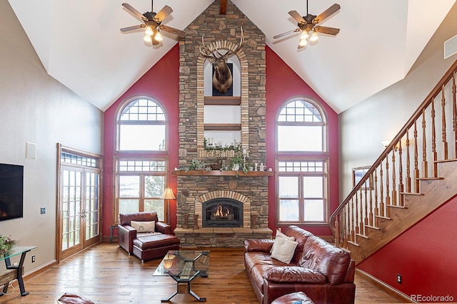 living area featuring plenty of natural light, a stone fireplace, wood finished floors, and a ceiling fan