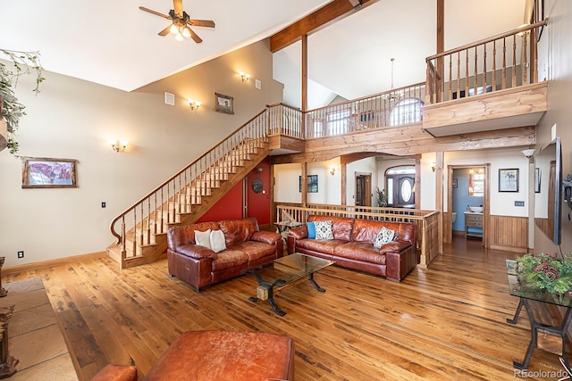 living room with beam ceiling, high vaulted ceiling, a ceiling fan, hardwood / wood-style floors, and stairway