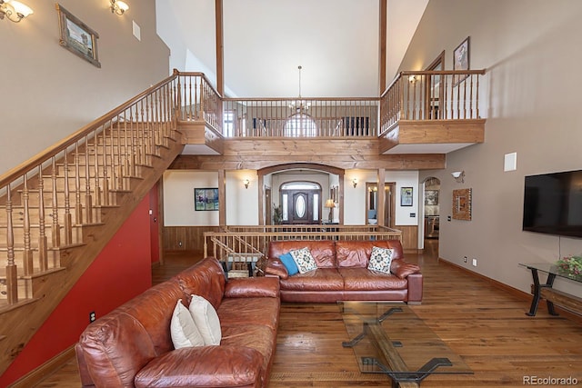 living room with arched walkways, stairway, a high ceiling, and hardwood / wood-style floors