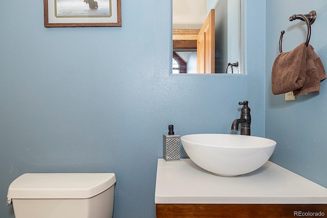 half bathroom featuring toilet, vanity, and a textured wall