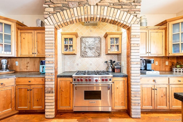 kitchen featuring wood finished floors, glass insert cabinets, luxury stove, and tasteful backsplash