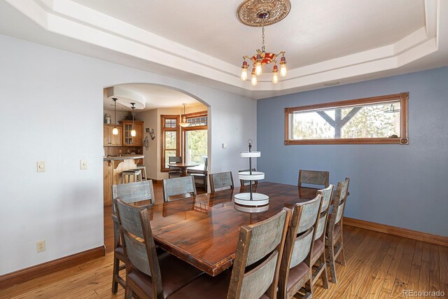 dining space with a raised ceiling, light wood-style floors, baseboards, and arched walkways