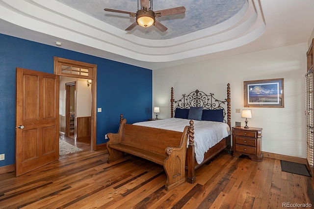 bedroom featuring baseboards, a raised ceiling, wood-type flooring, and a ceiling fan