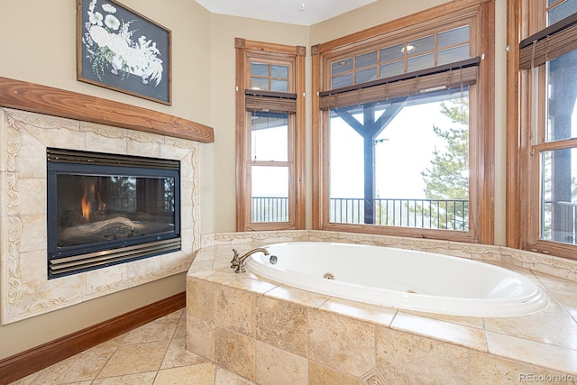 full bath with a high end fireplace, baseboards, stone tile flooring, and a whirlpool tub