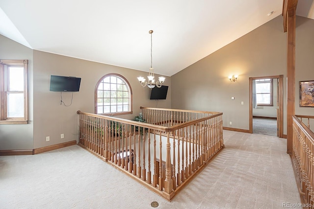 hall featuring high vaulted ceiling, light colored carpet, baseboards, and an inviting chandelier