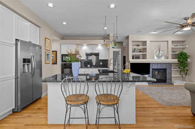 kitchen featuring a breakfast bar, sink, stainless steel fridge with ice dispenser, a kitchen island with sink, and white cabinets