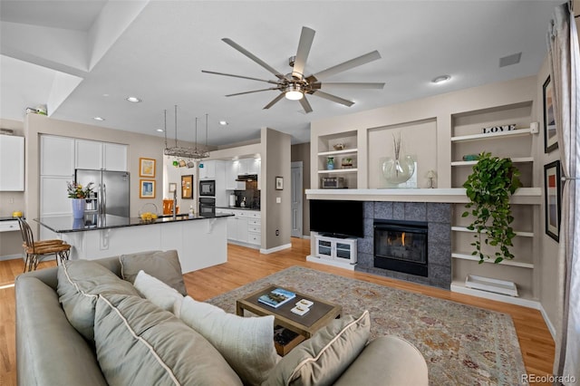 living room with ceiling fan, a tile fireplace, light hardwood / wood-style floors, and built in features