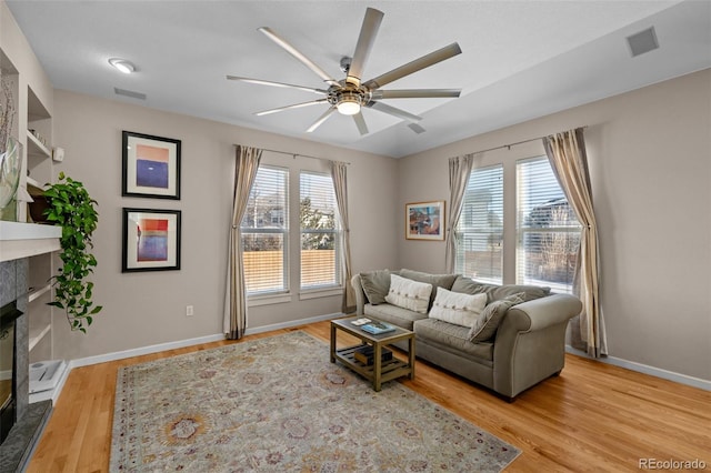 living room with a tile fireplace, ceiling fan, and light hardwood / wood-style floors