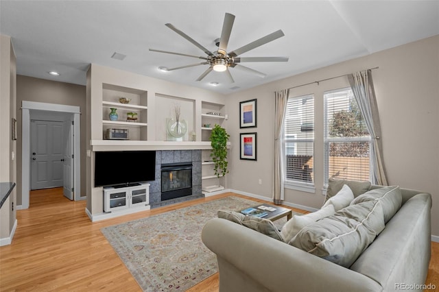 living room featuring a tile fireplace, ceiling fan, light hardwood / wood-style floors, and built in shelves