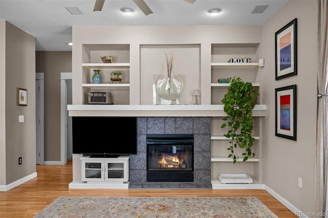 unfurnished living room featuring a tiled fireplace, hardwood / wood-style floors, ceiling fan, and built in shelves