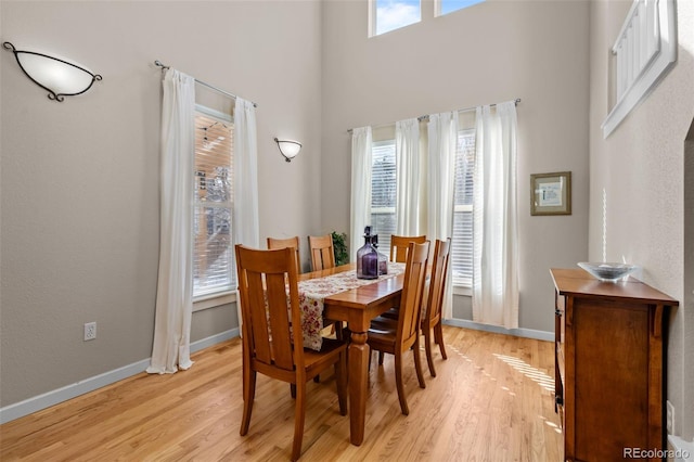 dining room with a high ceiling, a wealth of natural light, and light hardwood / wood-style flooring